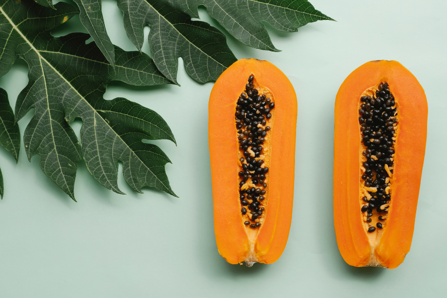 two halves of a papaya next to plant leaves