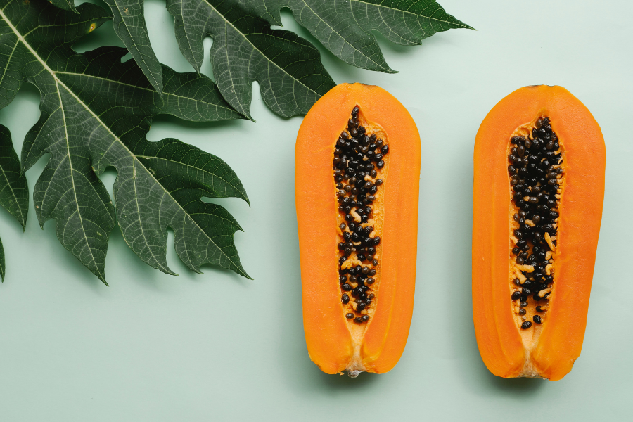 two halves of a papaya next to plant leaves 